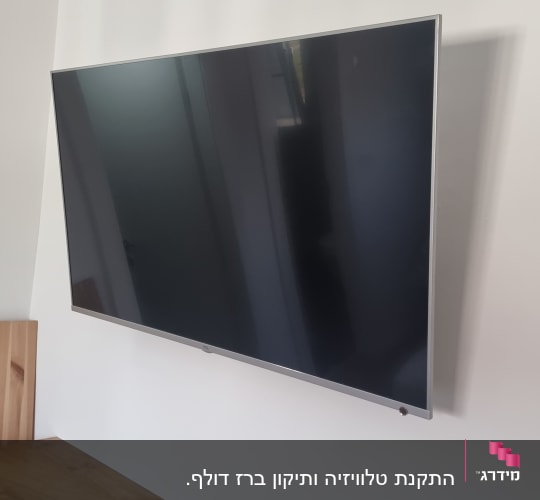 טלוויזיה מותקנת על קיר עם שלט על השידה